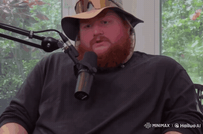 A Man With A Beard Is Sitting In Front Of A Microphone That Says Hailuo Ai On The Bottom Right GIF