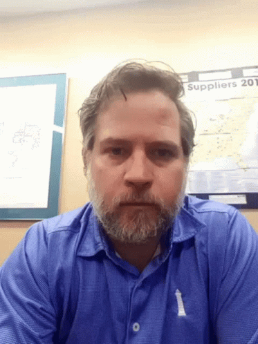 A Man With A Beard Is Sitting In Front Of A Poster That Says Suppliers GIF