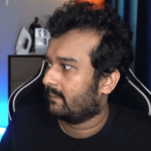 A Man With A Beard Is Sitting In Front Of A Sign That Says Go On GIF