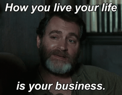 A Man With A Beard Is Sitting In Front Of A Sign That Says " How You Live Your Life Is Your Business " GIF