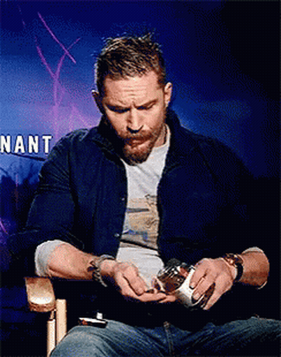 A Man With A Beard Is Sitting In Front Of A Sign That Says Nant . GIF