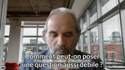 A Man With A Beard Is Sitting In Front Of A Window And Says Comment Peut-On Poser Une Question Aussi Debile GIF