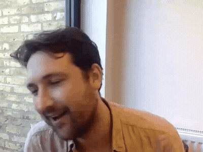 A Man With A Beard Is Sitting In Front Of A Window . GIF