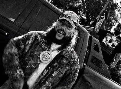 A Man With A Beard Is Sitting In The Back Of A Truck With A Gun . GIF