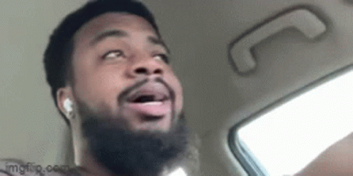 A Man With A Beard Is Sitting In The Back Seat Of A Car And Making A Funny Face . GIF