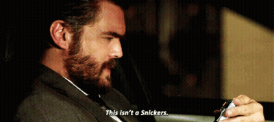 A Man With A Beard Is Sitting In The Back Seat Of A Car Holding A Snickers Bar . GIF