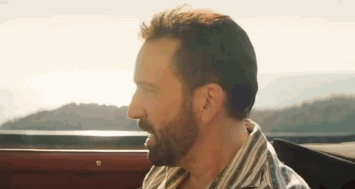 A Man With A Beard Is Sitting In The Back Seat Of A Car Looking Out The Window . GIF