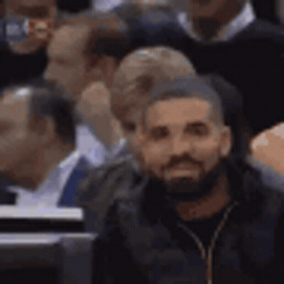 A Man With A Beard Is Sitting In The Stands At A Basketball Game . GIF