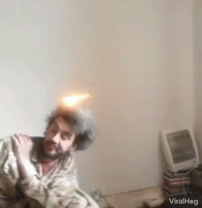 A Man With A Beard Is Sitting On A Bed With A Fireball In His Hair . GIF