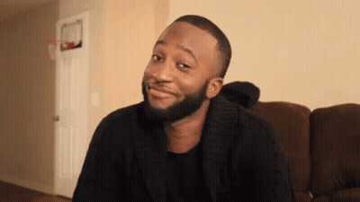 A Man With A Beard Is Sitting On A Couch And Smiling GIF