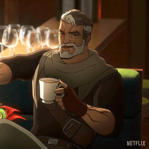 A Man With A Beard Is Sitting On A Couch Holding A Cup Of Coffee With A Netflix Logo In The Background GIF
