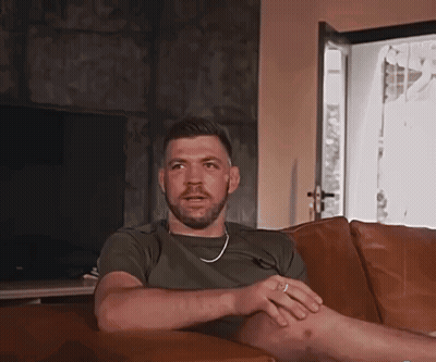 A Man With A Beard Is Sitting On A Couch In Front Of A Television GIF