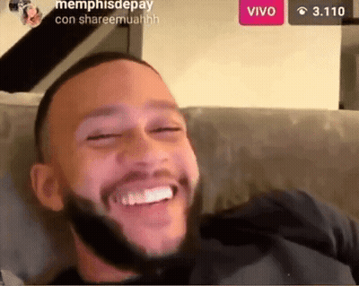 A Man With A Beard Is Sitting On A Couch Smiling GIF