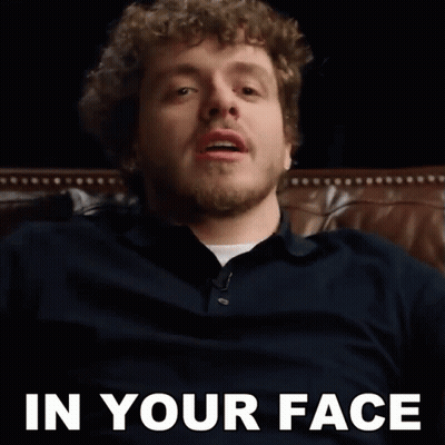 a man with a beard is sitting on a couch with the words in your face behind him