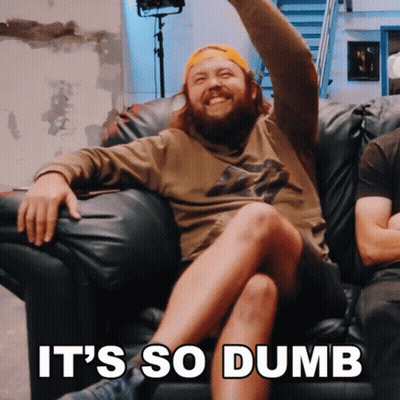 A Man With A Beard Is Sitting On A Couch With The Words It 'S So Dumb Behind Him GIF