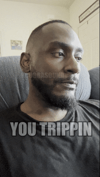A Man With A Beard Is Sitting On A Couch With The Words You Trippin On His Face GIF