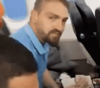 A Man With A Beard Is Sitting On A Plane Looking At Something . GIF