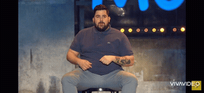 A Man With A Beard Is Sitting On A Stool In Front Of A Blue Sign That Says Vivavideo GIF