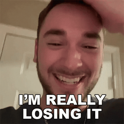 A Man With A Beard Is Smiling And Holding His Head . GIF