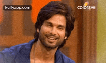 A Man With A Beard Is Smiling And Looking At The Camera While Wearing A Blue Shirt . GIF