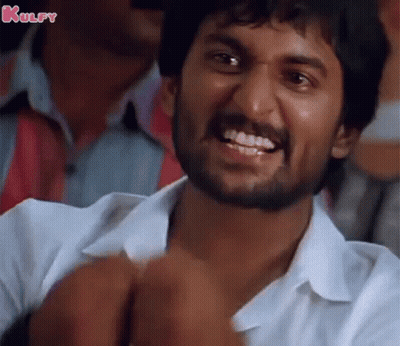 A Man With A Beard Is Smiling And Making A Funny Face While Sitting In A Crowd . GIF
