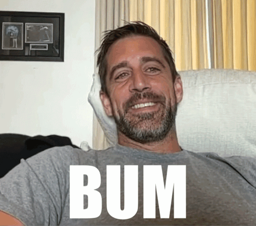 a man with a beard is smiling and wearing a shirt that says bum on it