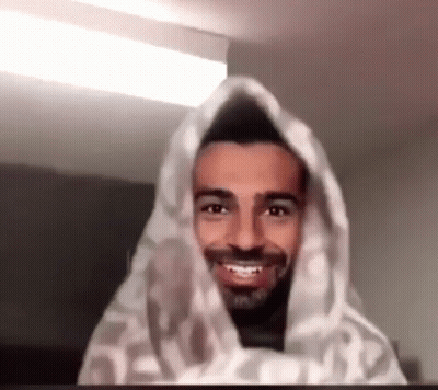 A Man With A Beard Is Smiling And Wrapped In A Blanket . GIF