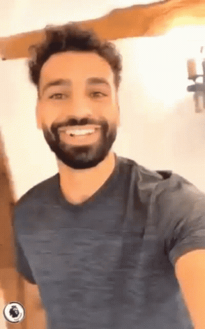 A Man With A Beard Is Smiling For The Camera While Wearing A Blue Shirt . GIF