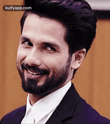 A Man With A Beard Is Smiling For The Camera While Wearing A Suit And Tie . GIF