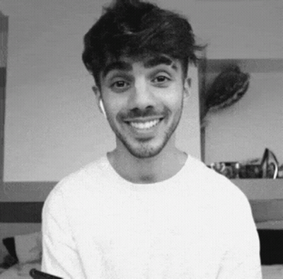 A Man With A Beard Is Smiling In A Black And White Photo While Wearing Headphones . GIF