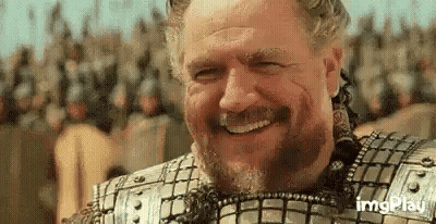 A Man With A Beard Is Smiling In Front Of A Crowd . GIF