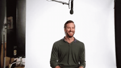 A Man With A Beard Is Smiling In Front Of A Microphone In A Studio . GIF