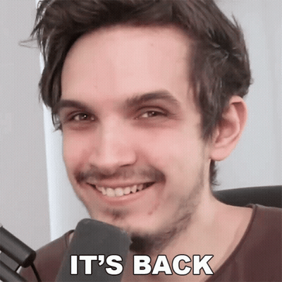 A Man With A Beard Is Smiling In Front Of A Microphone With The Words " It 'S Back " Written Below Him GIF