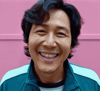 A Man With A Beard Is Smiling In Front Of A Pink Wall . GIF