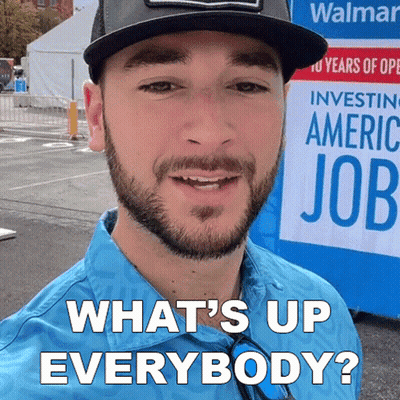 A Man With A Beard Is Smiling In Front Of A Sign That Says What 'S Up Everybody GIF