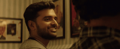 A Man With A Beard Is Smiling In Front Of A Wall With Pictures On It GIF