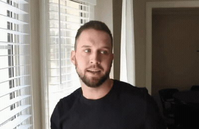 A Man With A Beard Is Smiling In Front Of A Window With Blinds GIF