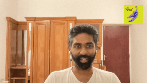 A Man With A Beard Is Smiling In Front Of A Yellow Sign That Says " Let 'S Play " GIF