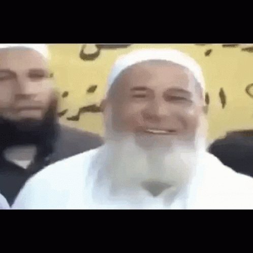 A Man With A Beard Is Smiling In Front Of Another Man GIF