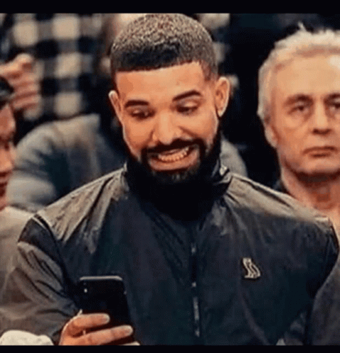 A Man With A Beard Is Smiling While Holding A Cell Phone In His Hand . GIF