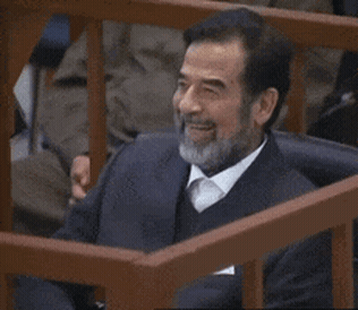 A Man With A Beard Is Smiling While Sitting Behind A Wooden Fence GIF