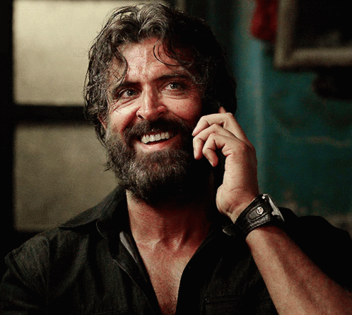 A Man With A Beard Is Smiling While Talking On A Phone GIF