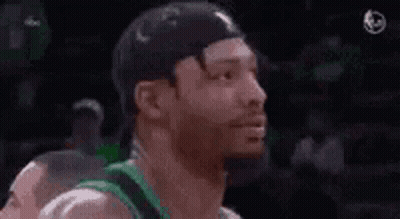 A Man With A Beard Is Smiling While Wearing A Green Jersey And A Hat . GIF