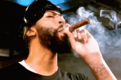 A Man With A Beard Is Smoking A Cigar With Smoke Coming Out Of His Mouth . GIF
