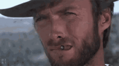 A Man With A Beard Is Smoking A Cigarette And Wearing A Cowboy Hat . GIF
