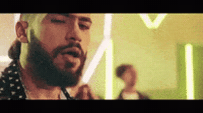 A Man With A Beard Is Smoking A Cigarette In A Room With Neon Lights . GIF
