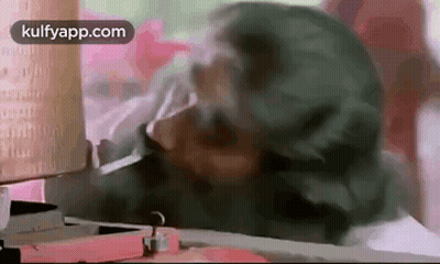 A Man With A Beard Is Smoking A Cigarette While Sitting At A Table . GIF
