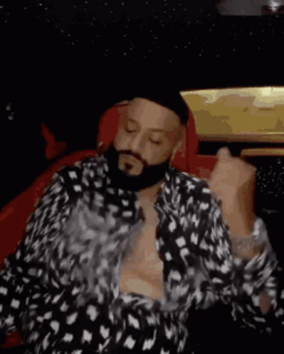 A Man With A Beard Is Smoking A Cigarette While Sitting In A Car With His Shirt Off . GIF
