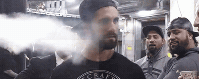 A Man With A Beard Is Smoking An Electronic Cigarette In Front Of A Group Of People . GIF