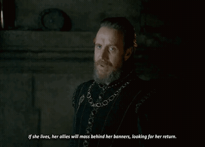 A Man With A Beard Is Standing In A Dark Room And Talking To Another Man . GIF